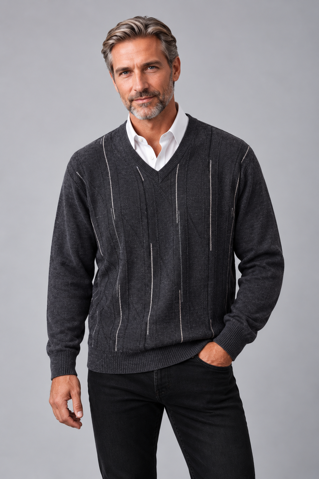A man wearing a dark gray v-neck sweater with vertical white stripe details, layered over a white collared shirt and paired with black pants, against a solid gray studio background.