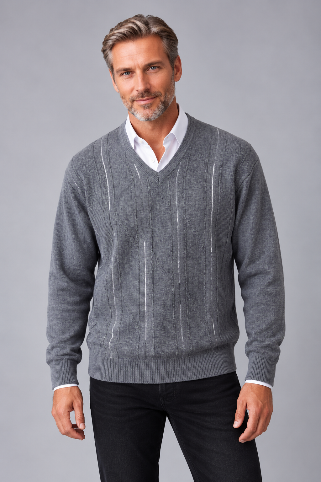 A man wearing a gray v-neck sweater with vertical knit stripe details over a white collared shirt and black pants, photographed against a solid gray studio background.