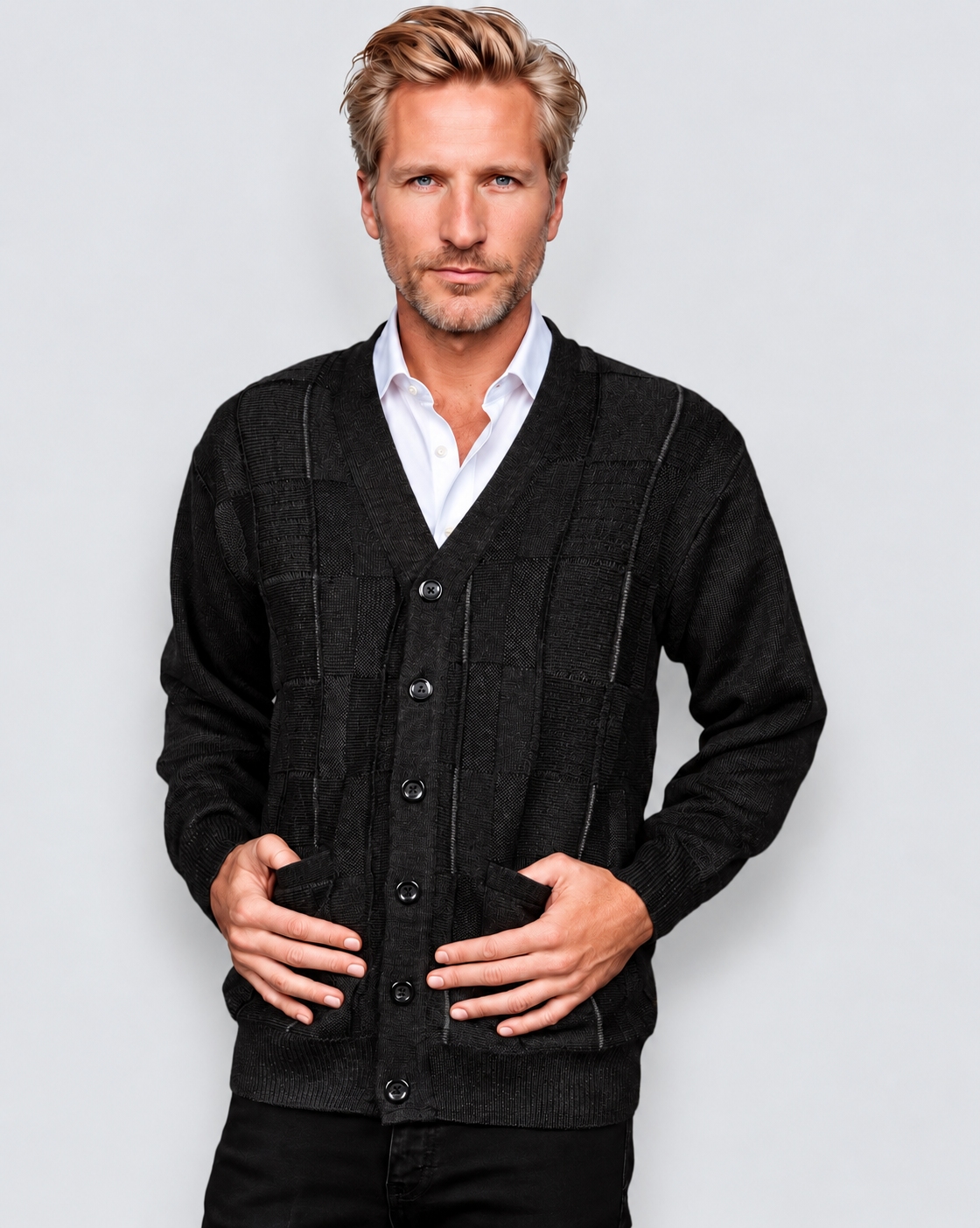 A man wearing a dark charcoal gray knit cardigan sweater over a white collared shirt, standing against a light gray studio background.