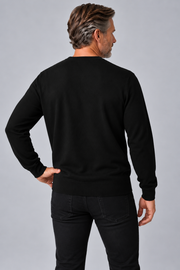 A man shown from the back wearing a black long-sleeve crewneck sweater and black jeans, standing against a solid gray studio background.