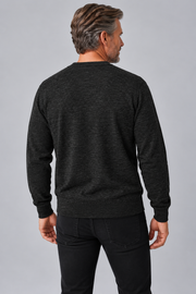 A man viewed from the back wearing a dark charcoal gray long-sleeve crewneck sweater and black jeans, standing against a solid gray studio background.