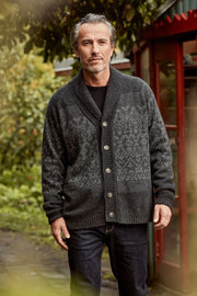 A man wearing a dark gray patterned knit cardigan over a black shirt and dark jeans, standing outdoors in front of a red telephone booth.