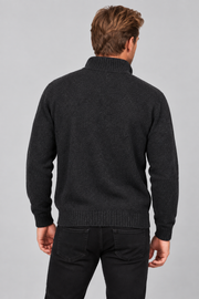 A man viewed from behind wearing a dark charcoal gray ribbed knit sweater and black pants, against a solid light gray studio background.