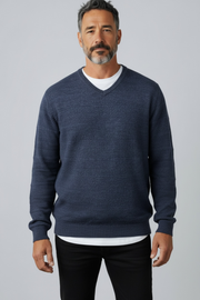 Man wearing a navy blue sweater over a white shirt on a gray background