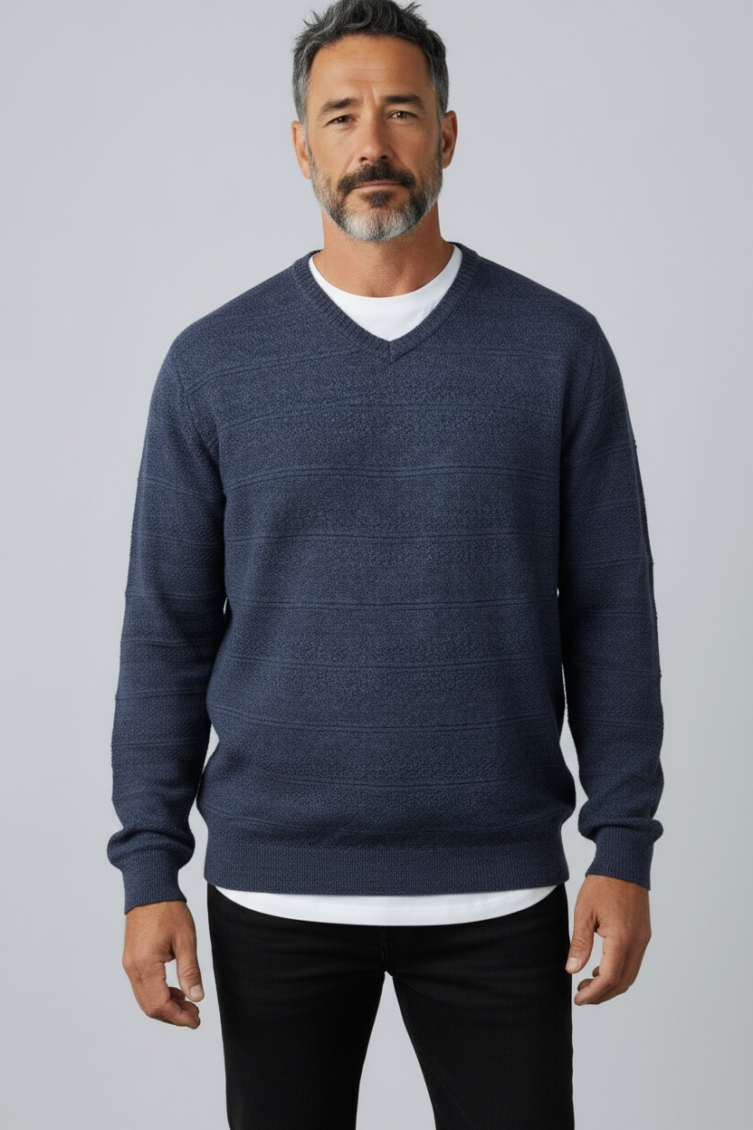 Man wearing a navy blue sweater over a white shirt on a gray background