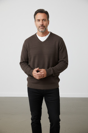 Man wearing a brown sweater and black pants against a plain background
