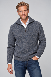 A man wearing a dark gray heathered knit quarter-zip pullover sweater over a white collared shirt and blue jeans, standing against a light gray studio background.