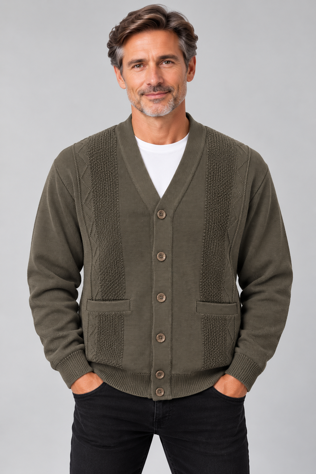 A man wearing an olive green knit cardigan with textured panels and button-front closure, layered over a white t-shirt and black pants, against a solid gray studio background.