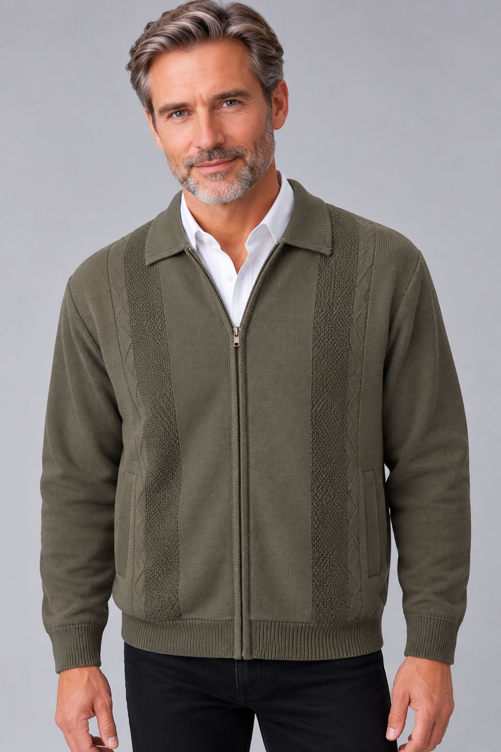 A man wearing an olive green zip-up knit sweater with textured vertical panels, styled over a white collared shirt and dark pants, against a solid gray studio background.