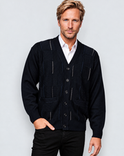 A man wearing a dark navy blue knit cardigan vest over a white collared shirt and black pants, standing against a light gray studio background.