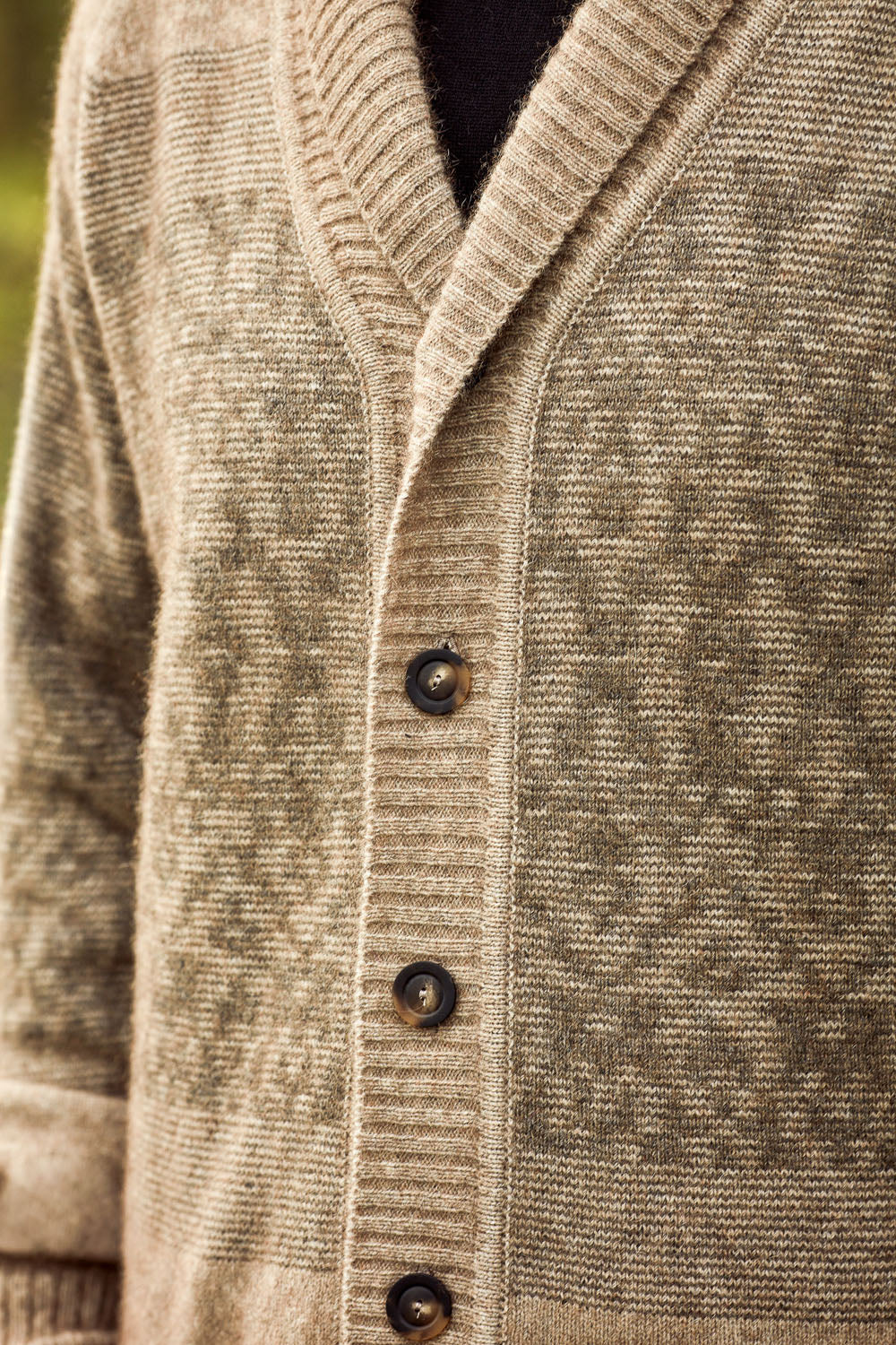 Close-up of a textured knit cardigan sweater in a warm taupe-beige color, featuring a V-neck, dark brown buttons, and a subtle woven pattern.