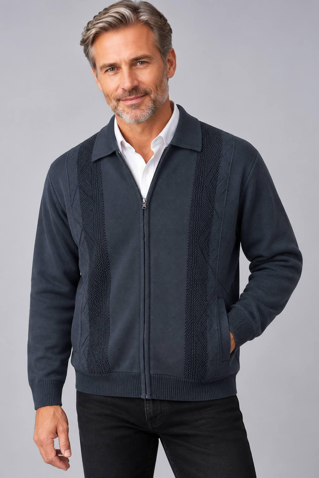 A man wearing a dark navy blue zip-up knit sweater with textured vertical panels over a white collared shirt and black pants, photographed against a solid gray studio background.