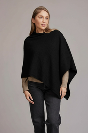 Woman wearing a black poncho over a sweater and jeans on a gray background