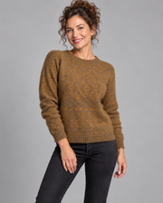 A woman modeling a brown and gold patterned knit sweater with black jeans, standing against a solid gray studio background.
