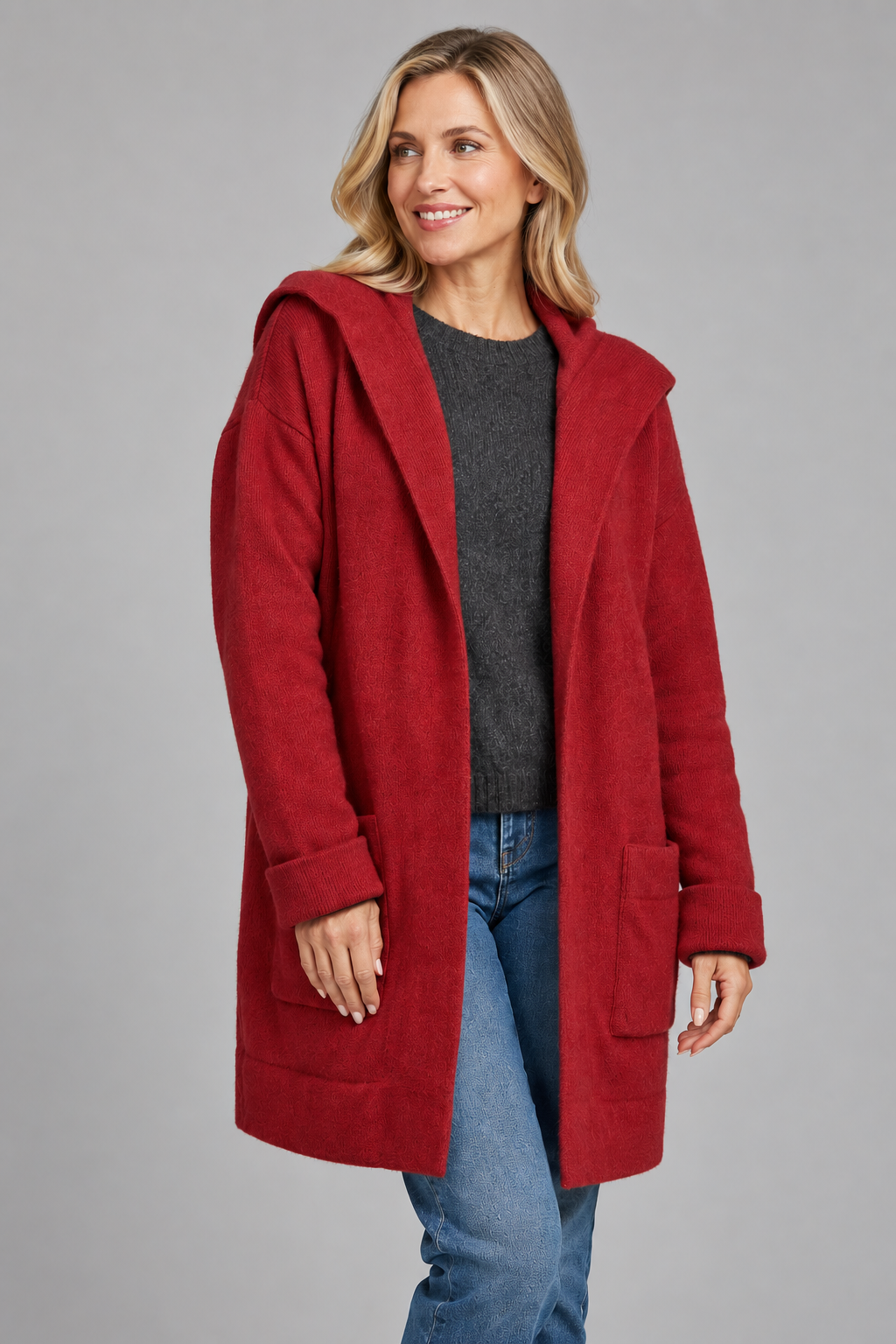 A woman modeling a red hooded coat over a dark gray sweater and blue jeans, photographed against a plain light gray studio background.