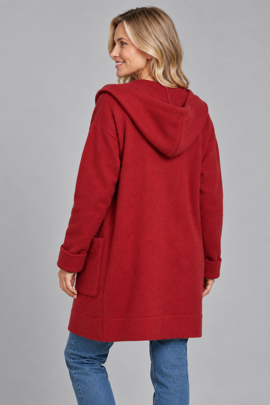 A woman wearing a red hooded coat, shown from the back, paired with blue jeans against a solid gray studio background.