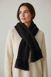 Woman wearing a black scarf with fringe on a plain background